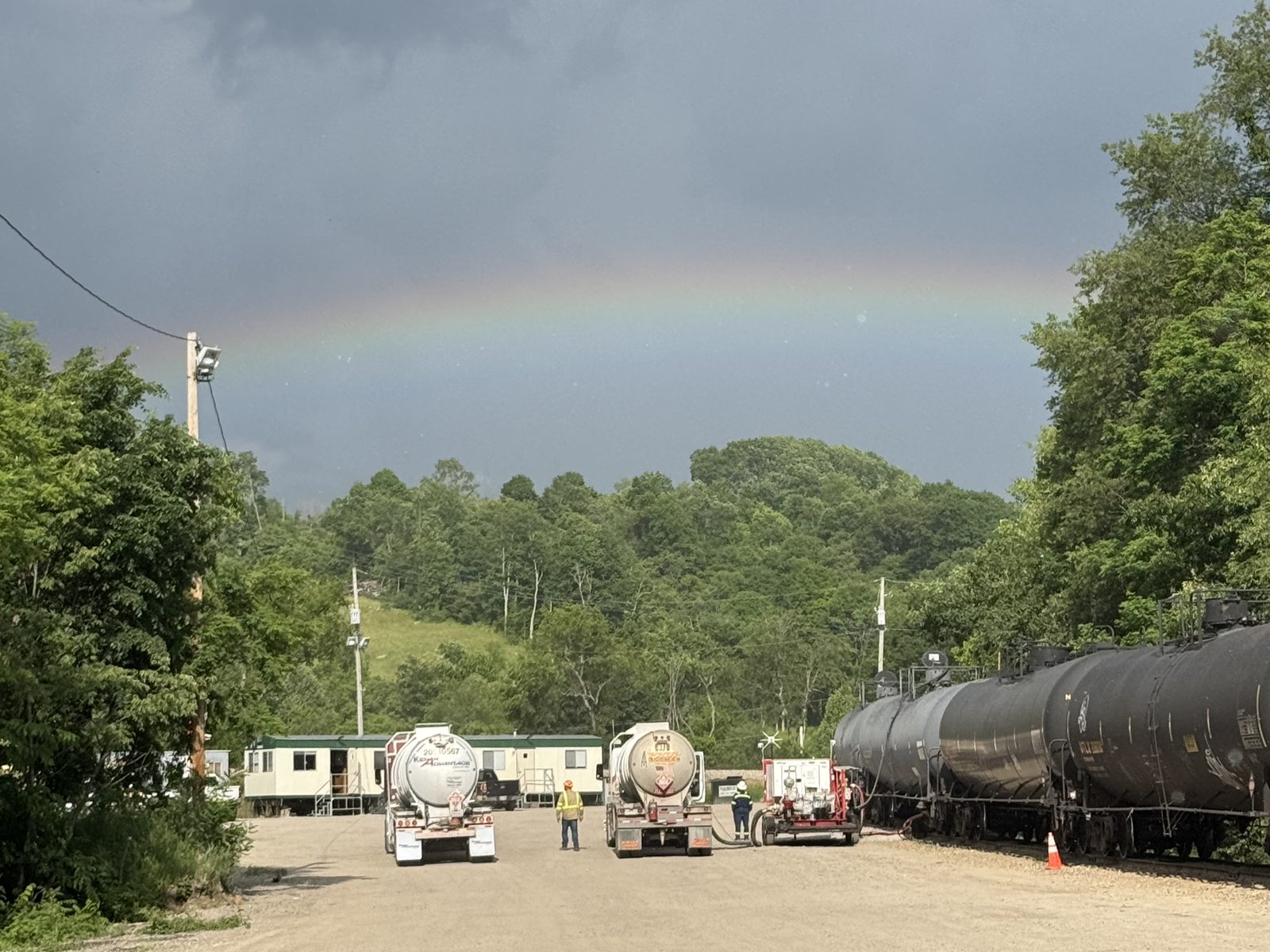 Tank trucks and rail tank cars at a crude truck-to-rail terminal under a rainbow